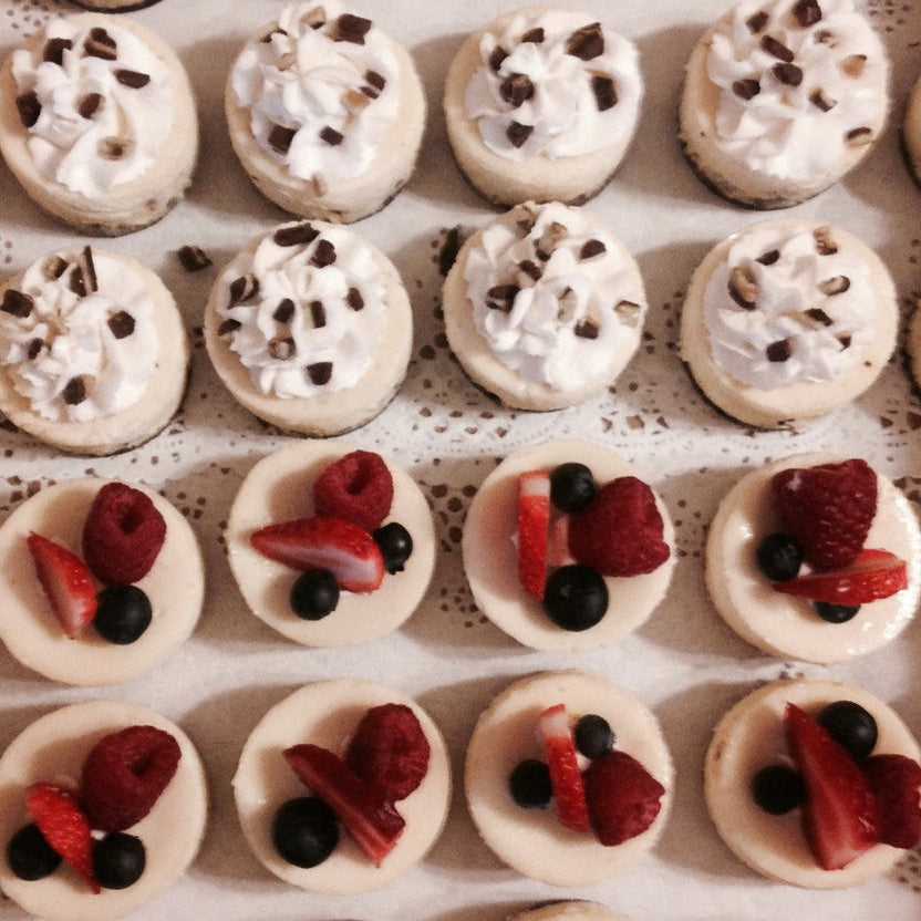 Small desserts with white cream and berries arranged in rows on a lace tablecloth.